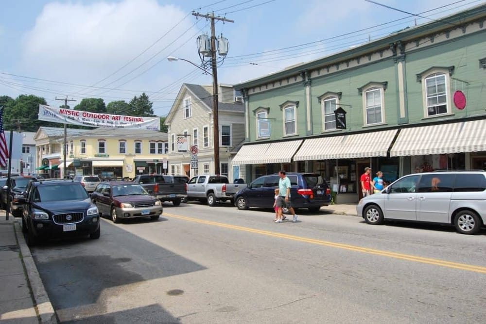 Colorful downtown street with parked vehicles, shops, and pedestrians in a charming small-town setting.