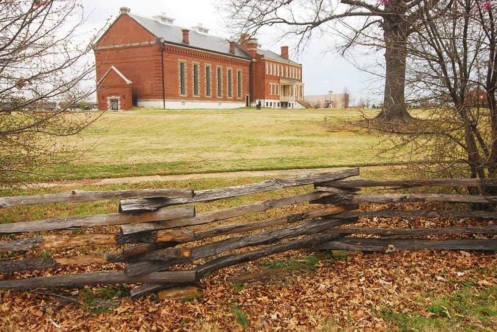Historic red brick building with wooden fence, fall leaves, and scenic landscape, QuestForDirections location.