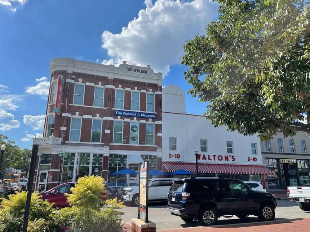 Colorful downtown street view featuring historic buildings, parking, and vibrant signage in a sunny setting.