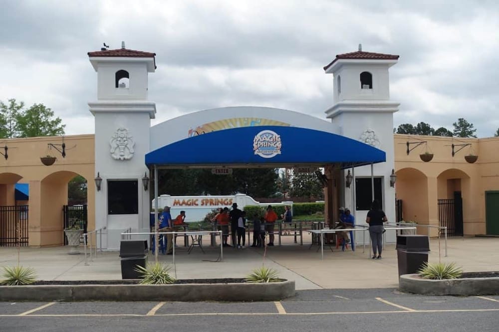 Amusement park entrance at Magic Springs with people waiting in line and a blue canopy overhead.