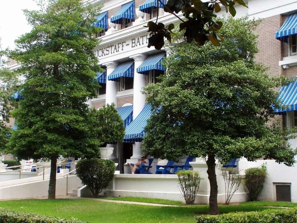 Elegant hotel exterior with blue striped awnings and lush greenery, featuring the QuestForDirections logo.