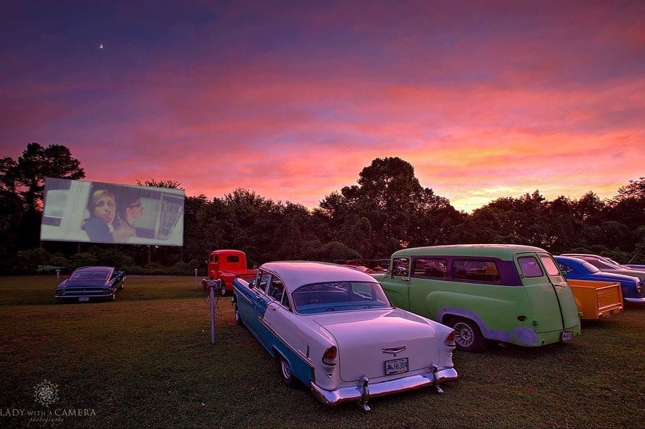 Classic cars and an outdoor drive-in movie under a colorful sunset sky, perfect for nostalgic cruising and outdoor entertainment.
