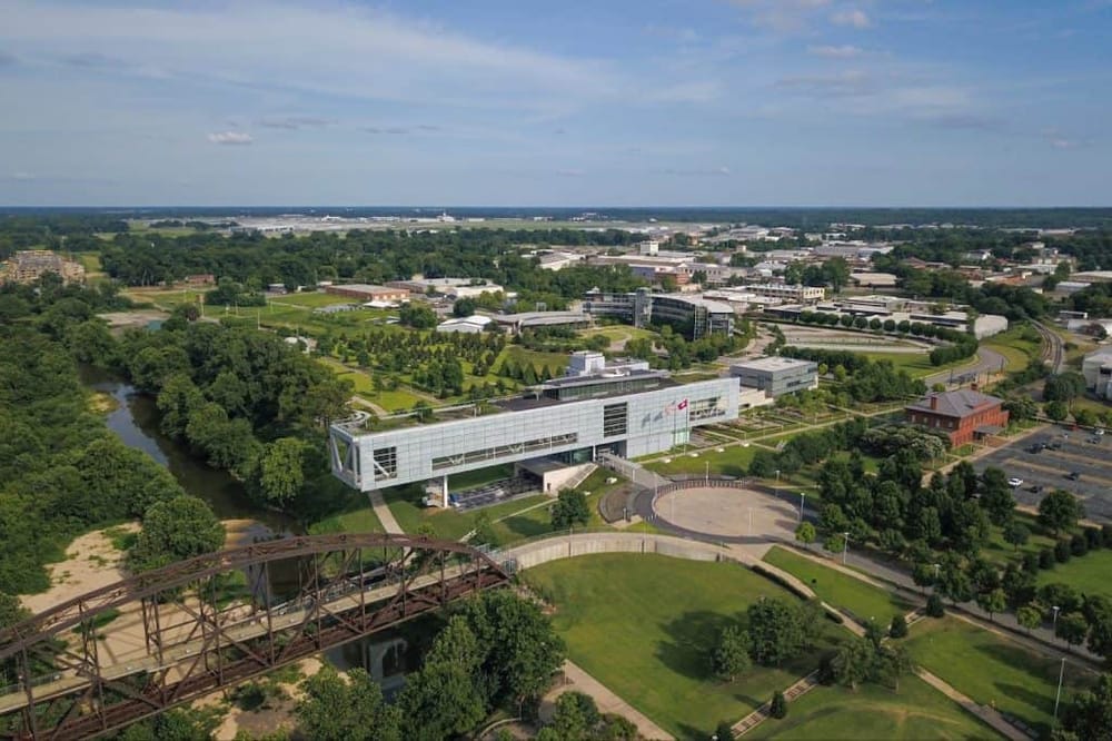 Modern corporate office building in a lush green park with walking paths and a creek, aerial view.