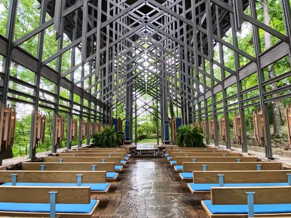 Modern glass chapel with open forest views, outdoor seating, and lush greenery, ideal for spiritual retreats and nature-inspired ceremonies.