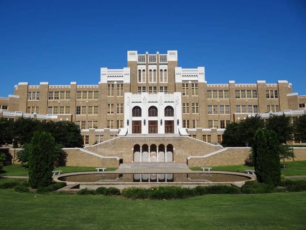 Historic high school building with classic architecture, lush green lawns, and a reflective pond.