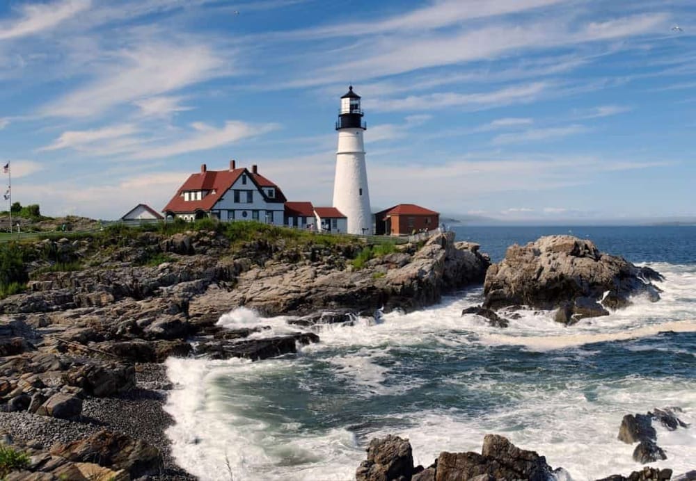Lighthouse near rocky coast with ocean waves in the background, scenic seaside travel destination.