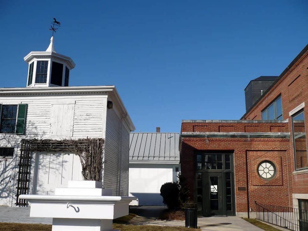 White historic building with weather vane and modern brick structure in the background.