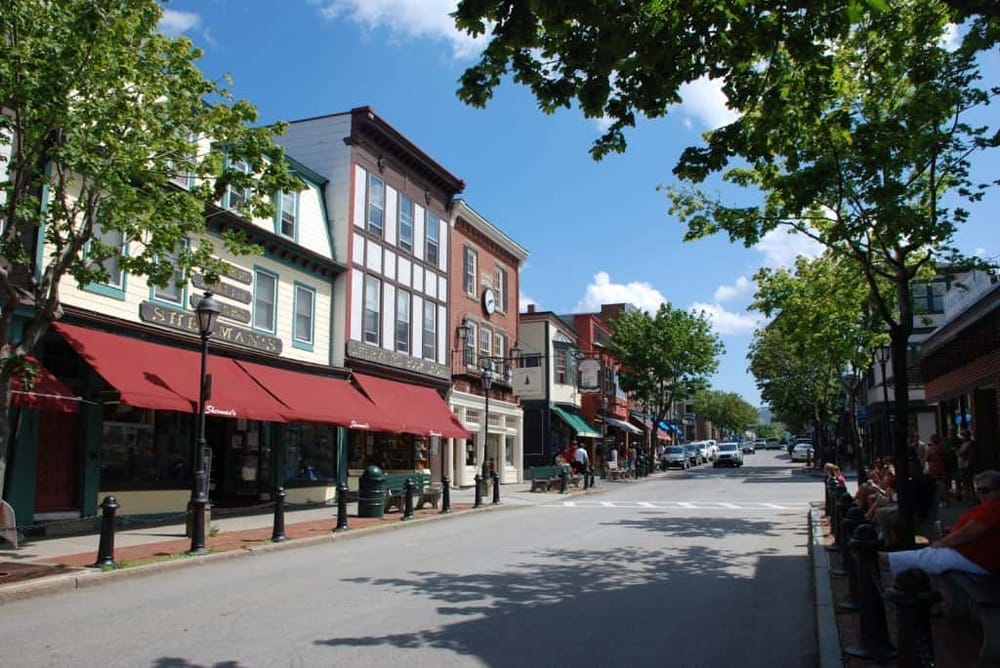 Charming downtown street with shops, cafes, and trees under a clear blue sky.