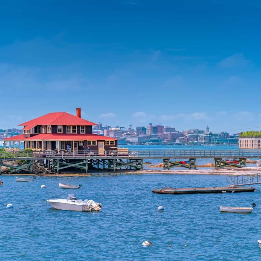 Charming waterfront house with a red roof and boat dock, overlooking a scenic city skyline.