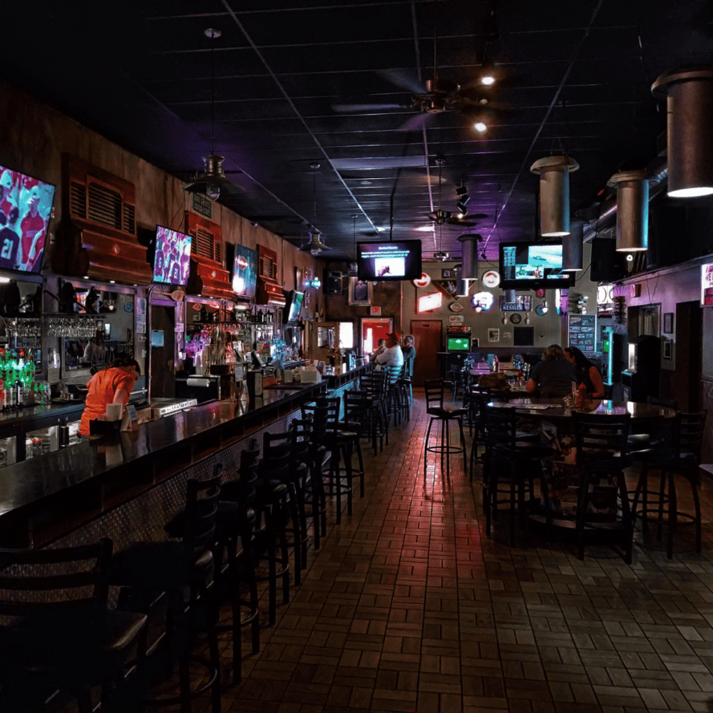 Cozy sports bar with multiple TVs, bar seating, and patrons enjoying drinks and live game coverage.