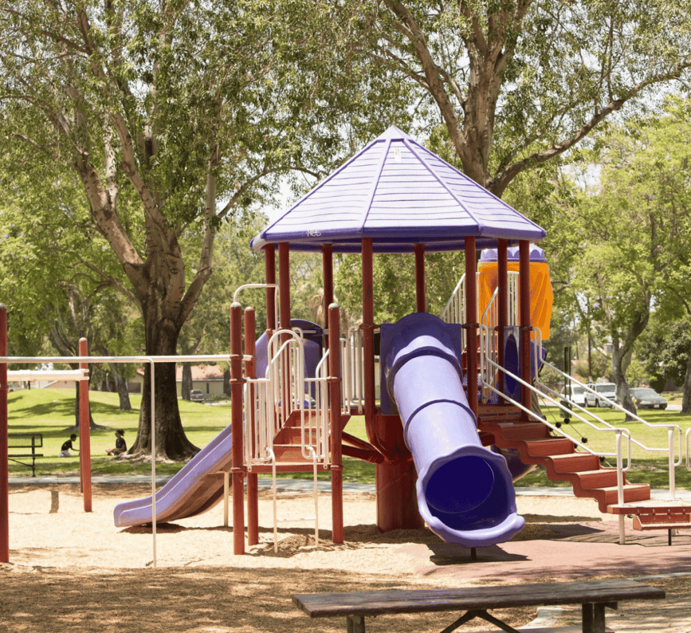 Colorful playground slide structure in a sunny park with trees and children playing.