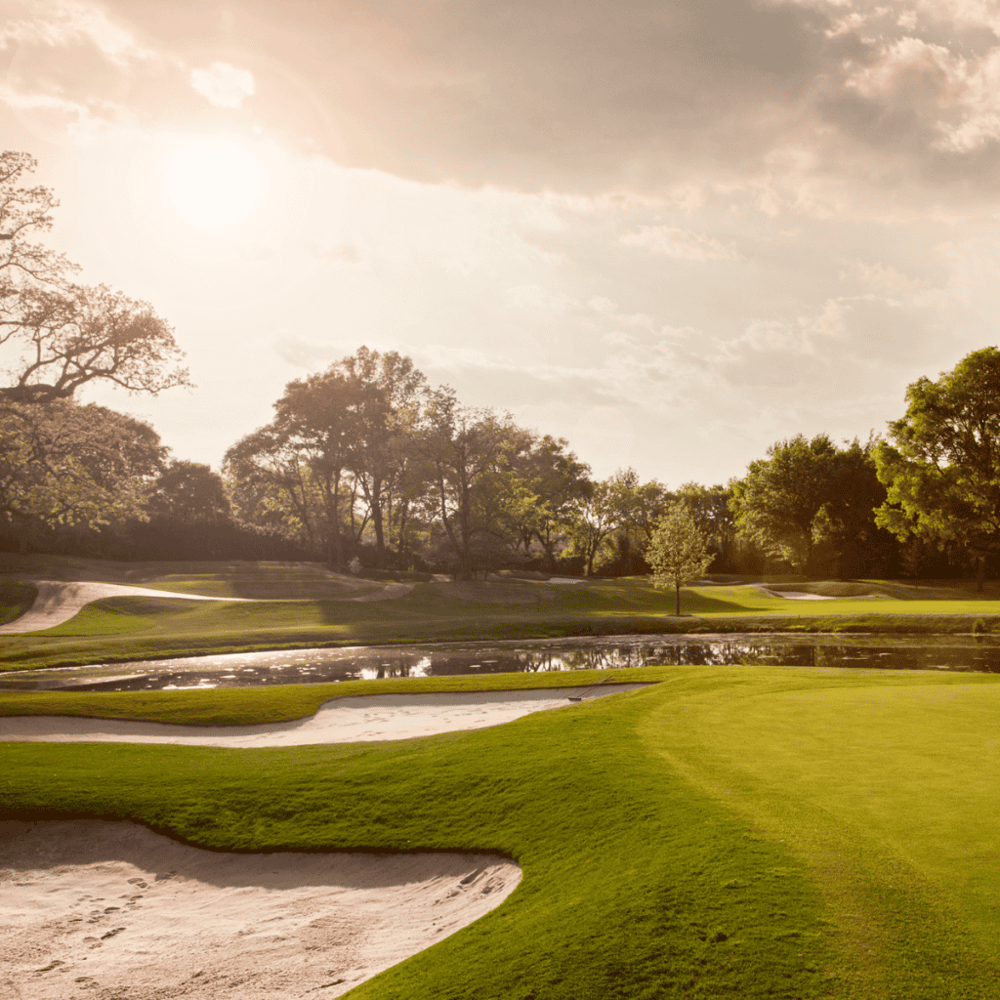 Lush green golf course with sand traps, water hazards, and trees under a bright, sunny sky.