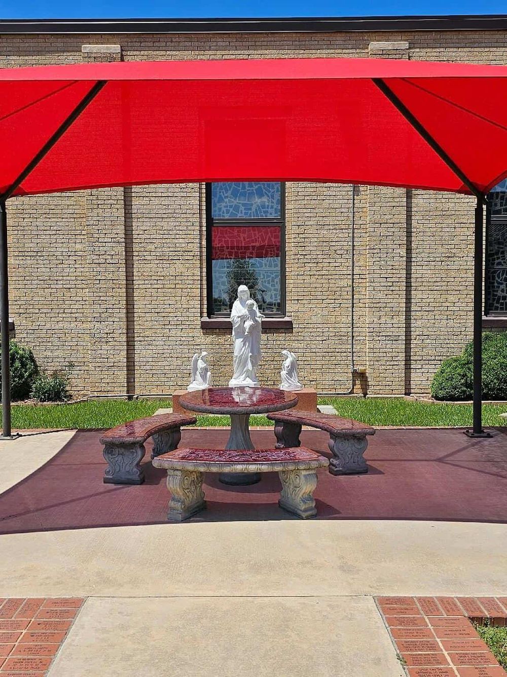 Relaxing outdoor seating area with statue, table, and benches under a red umbrella, near a brick building.
