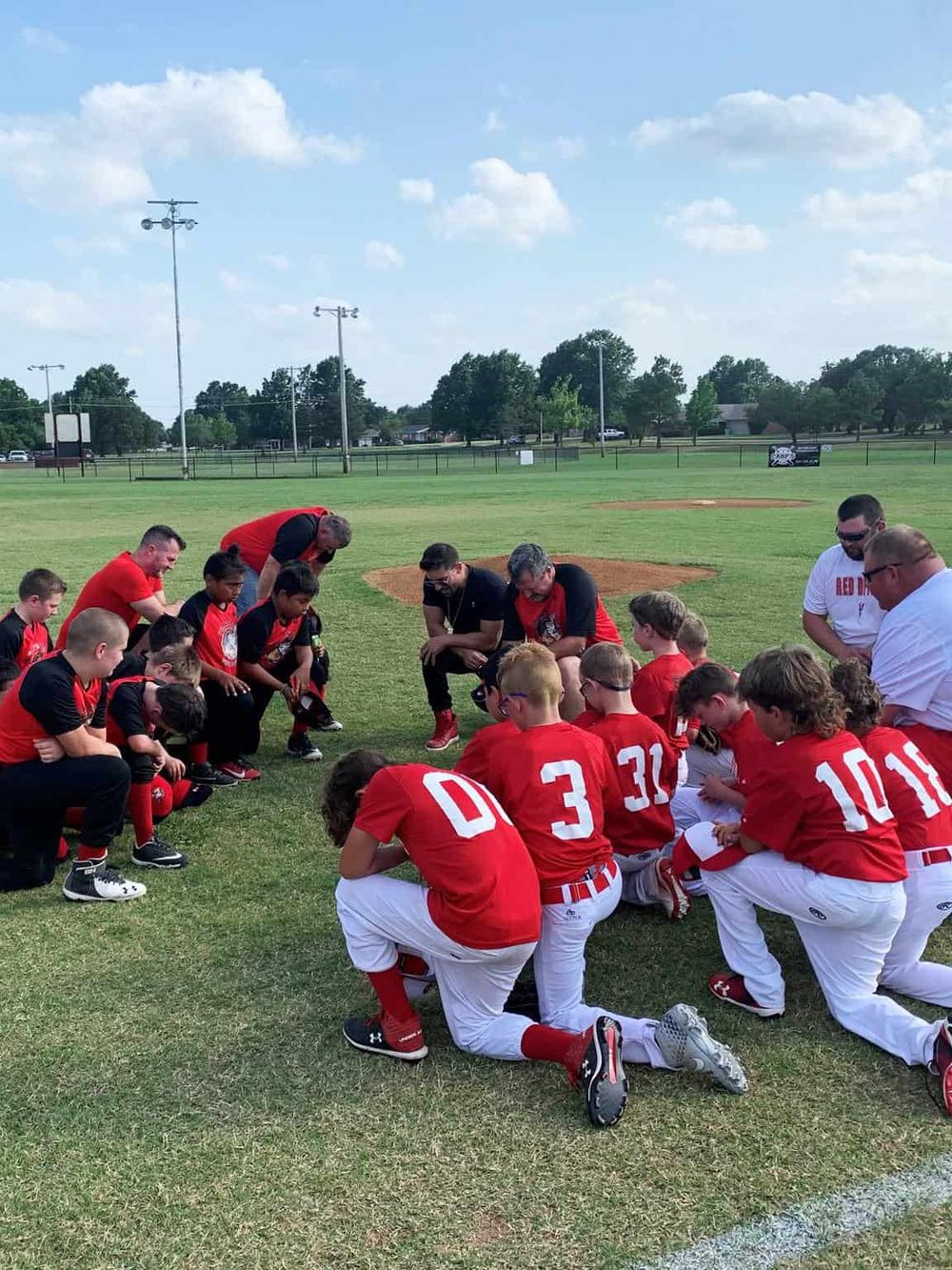 Team sports practice on a grass field, kids and coaches kneeling and listening attentively.