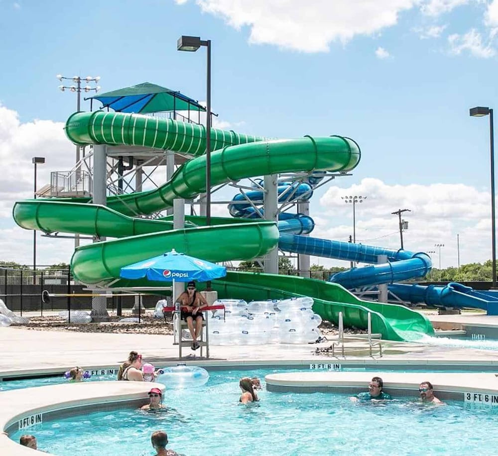 Bright green and blue water slides at a recreational water park with swimmers enjoying the pool area.