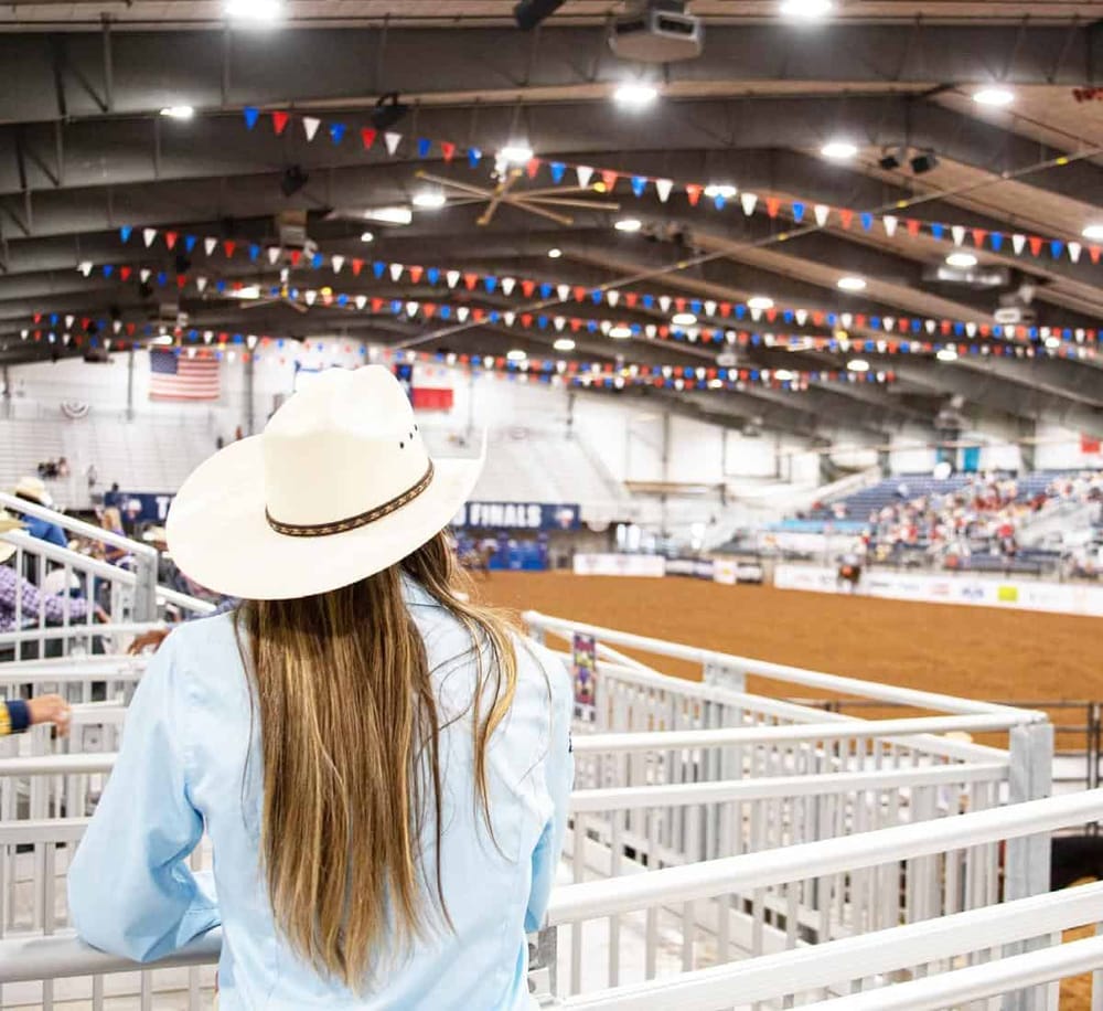 1. Wide-angle image of a person watching a rodeo event inside an indoor arena decorated with patriotic flags.