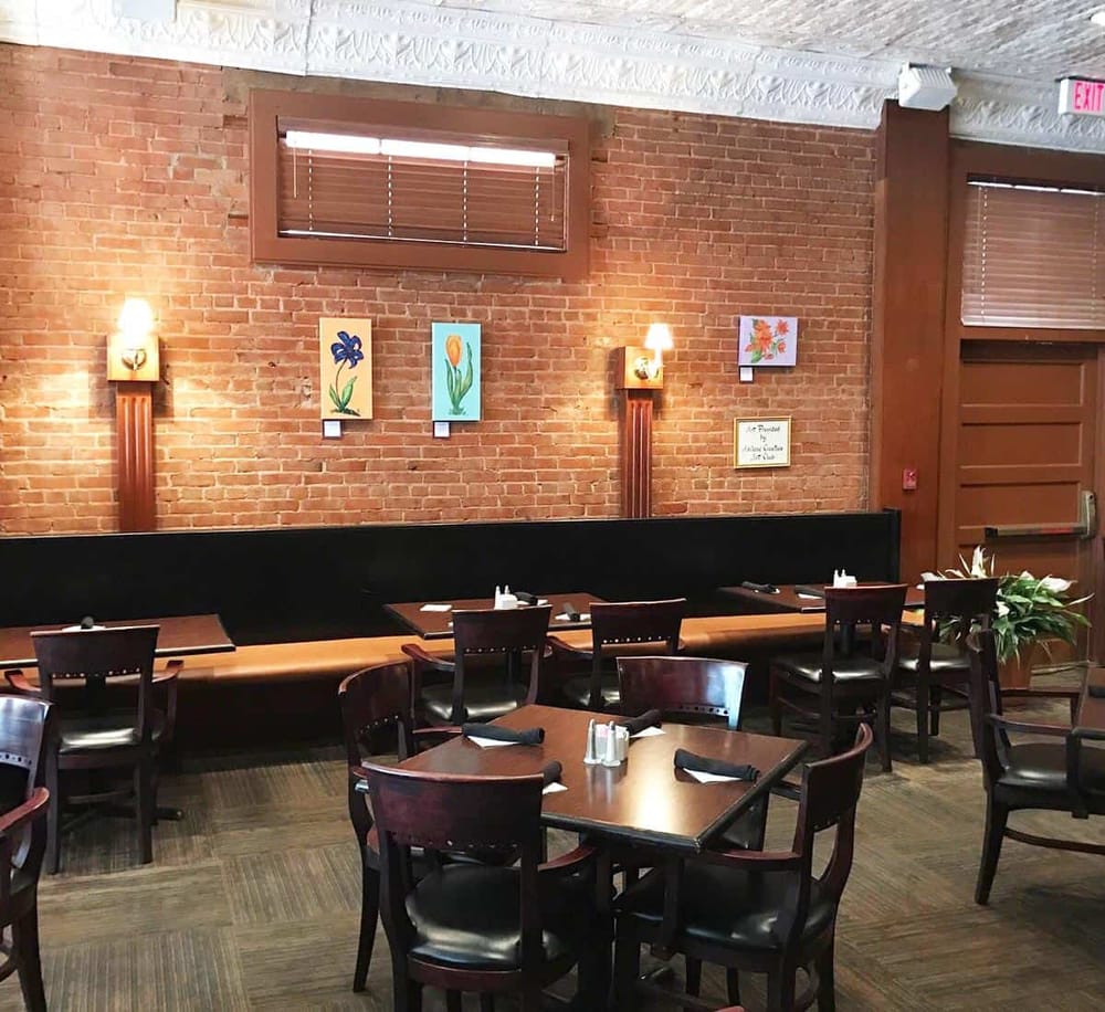 Cozy restaurant interior with brick walls, framed floral artwork, and wooden furniture for inviting dining experience.