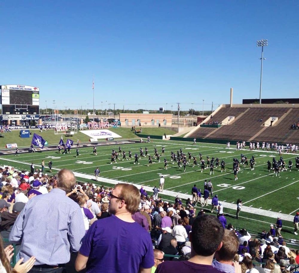 Vivid college football game at stadium with players, crowd, and sunny sky, showcasing sports event atmosphere.