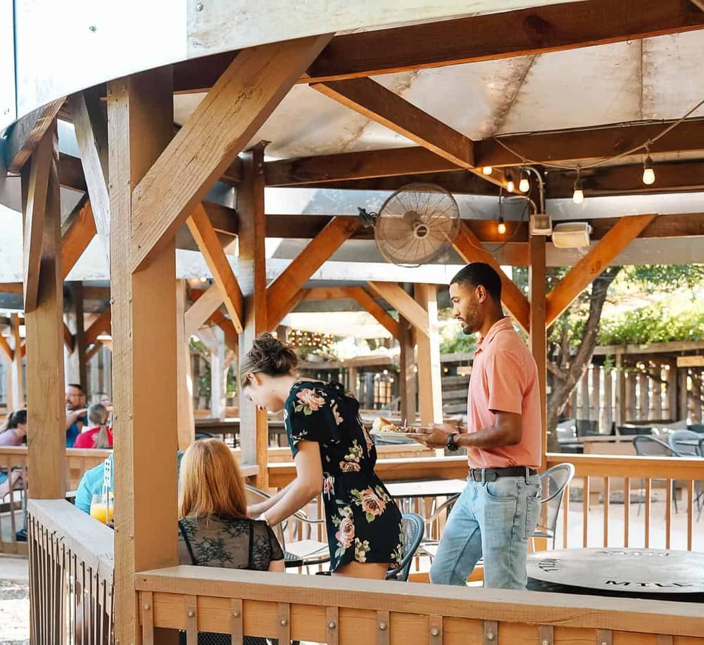 Friendly waiter serving food at an outdoor bar or restaurant patio.