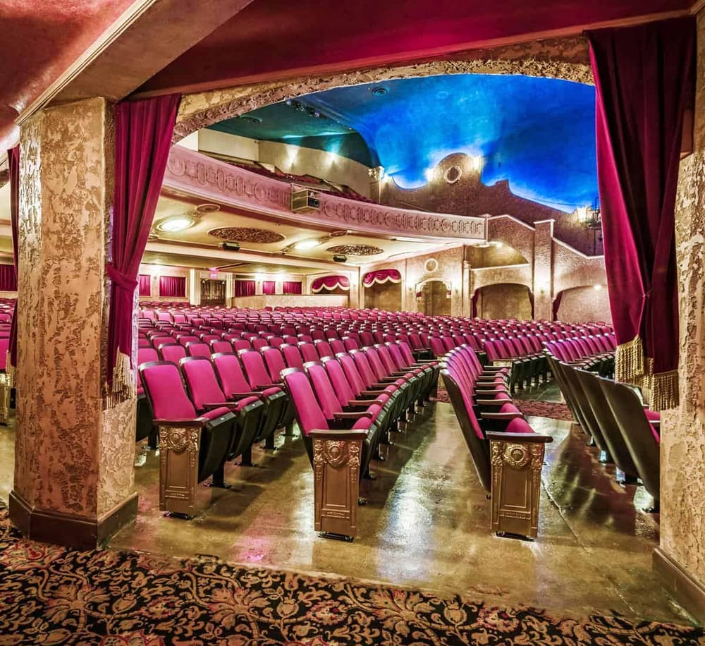 Luxurious theater seating with pink and black chairs, ornate decor, and a vibrant ceiling. Perfect for an elegant performance venue.