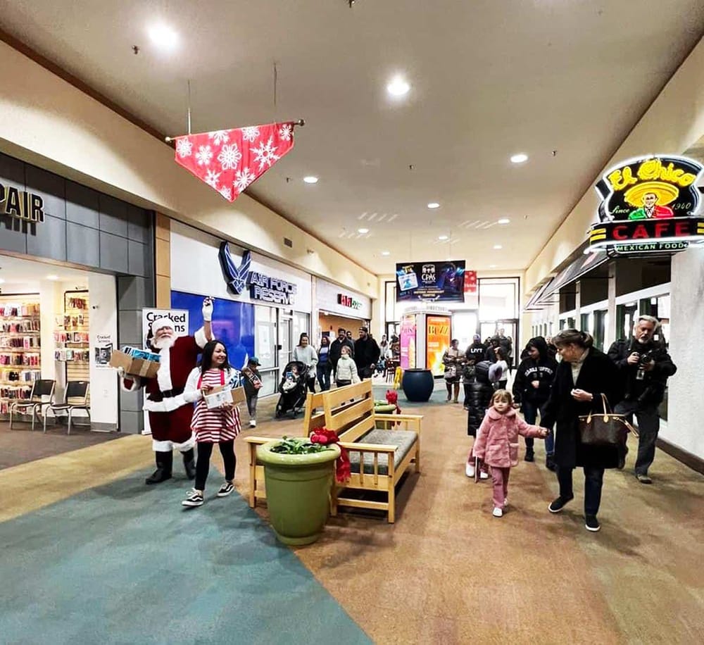 Festive holiday shopping mall with Santa Claus, shoppers, and holiday decorations in a busy retail center.