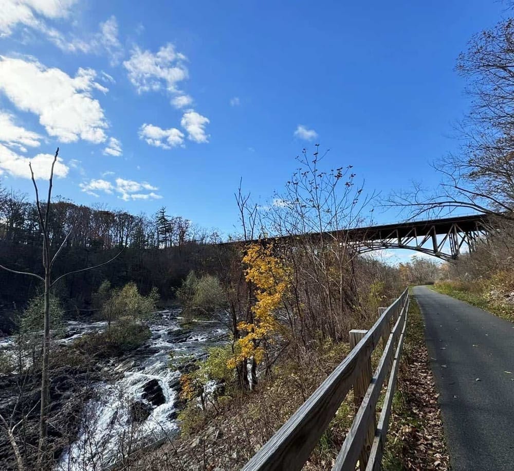 Scenic trail with river and bridge under clear blue sky, outdoor walking path in nature.