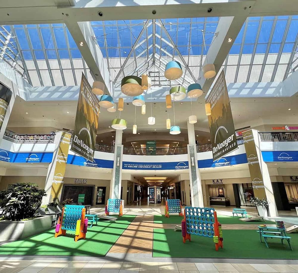 Bright indoor shopping mall atrium with colorful lighting fixtures and PlayStation Connect game area for kids.