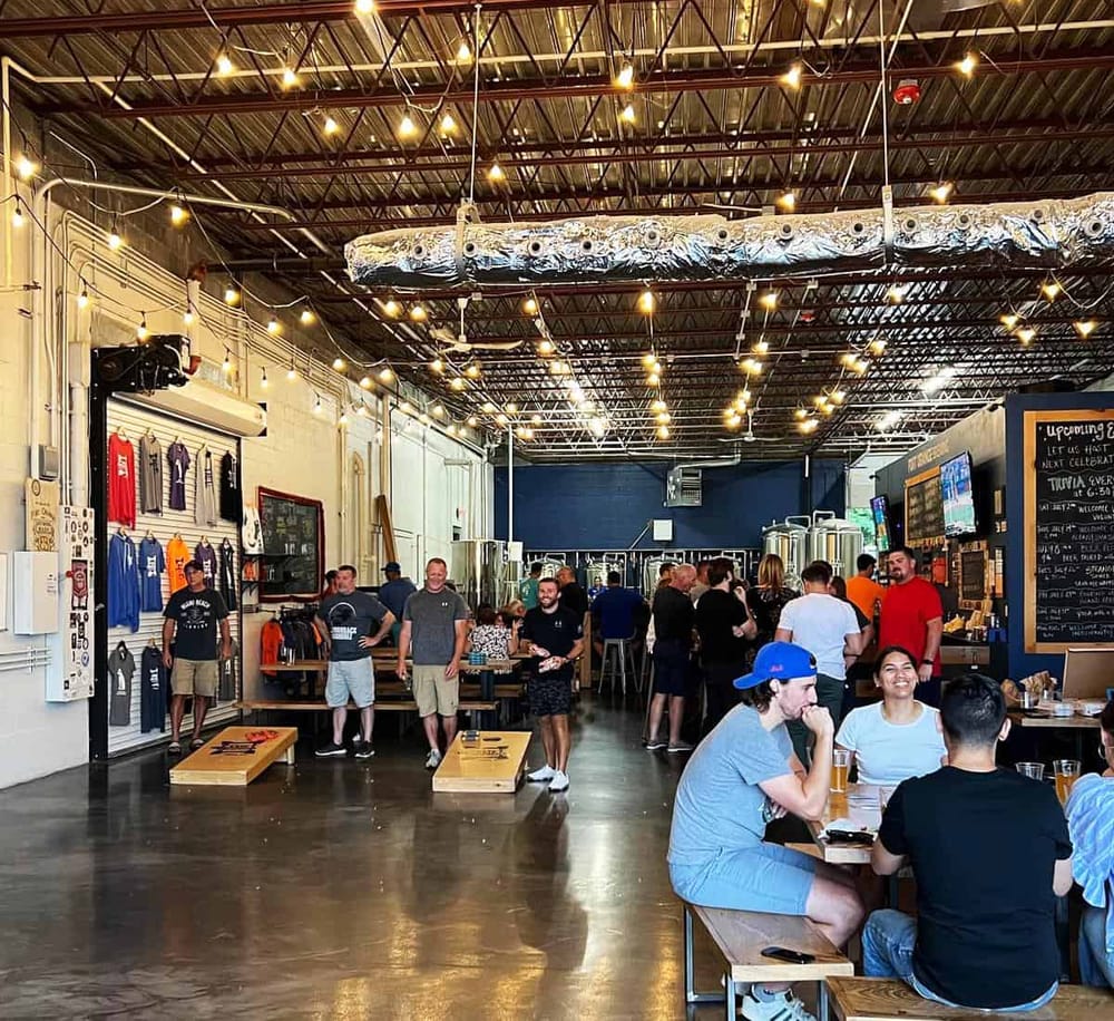 Bright indoor craft brewery with customers enjoying beer, merchandise, and vibrant lighting.