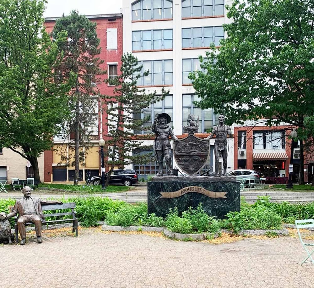 Historical statues in a city park with modern buildings in the background.