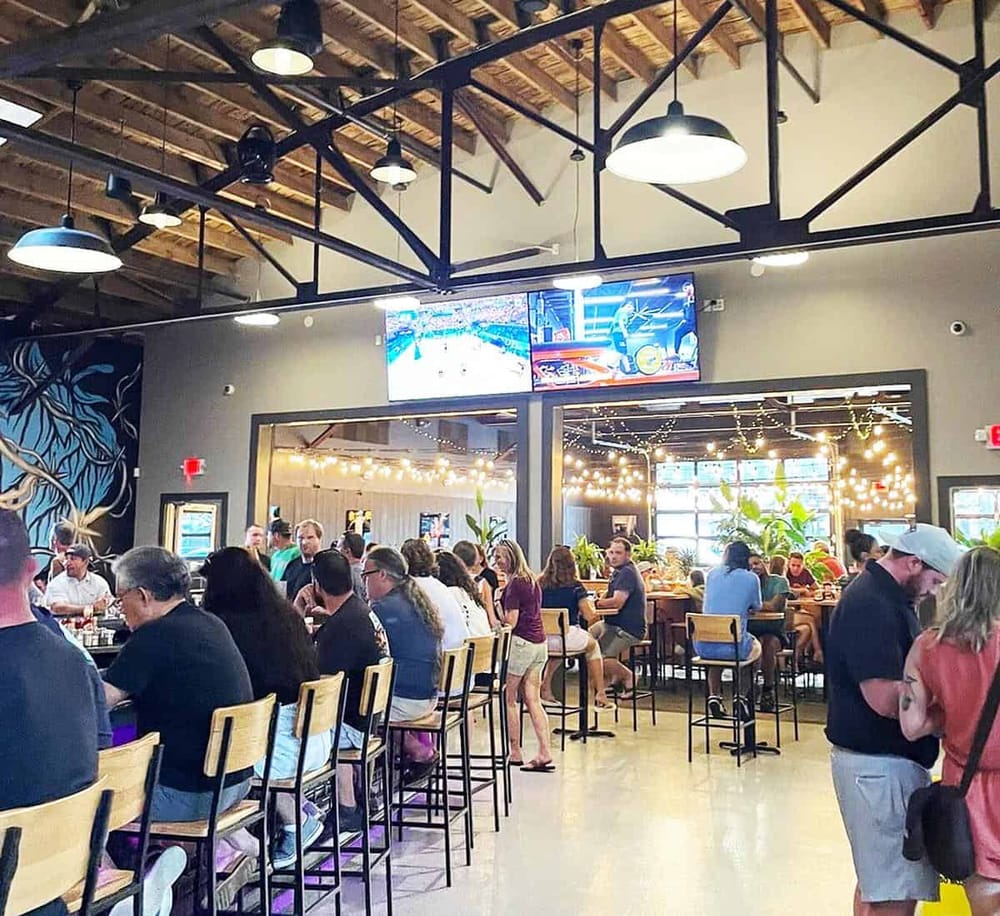 Modern bar interior with customers enjoying drinks and watching sports on LED screens.