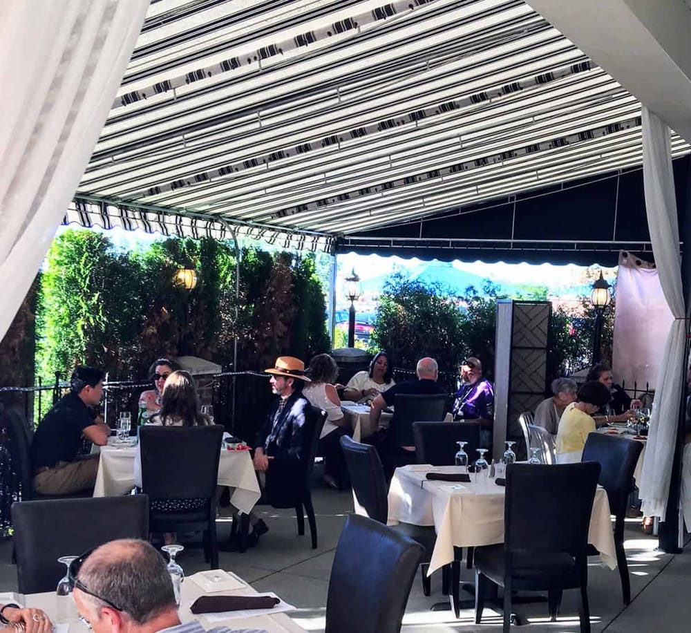 Outdoor dining at a restaurant with shaded patio, greenery, and elegant table settings.