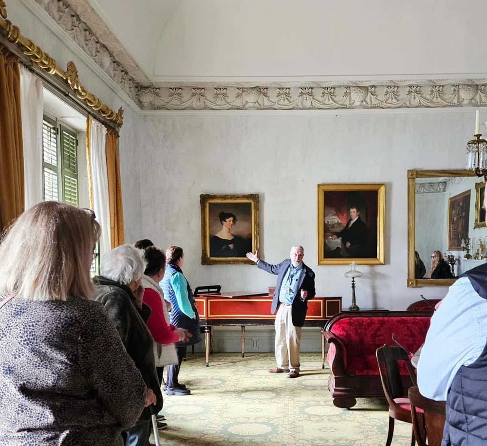 Historic estate tour with guide showcasing classic portraits in elegant interior.