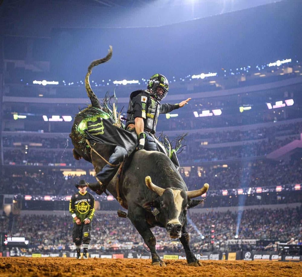 Fast-paced rodeo bull riding at nighttime arena with professional rider and digital crowd.