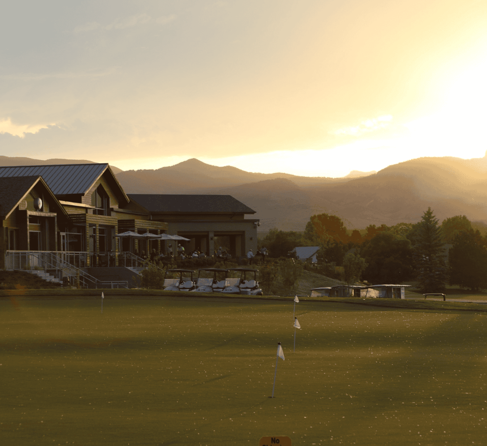 Golf course at sunset with clubhouse and scenic mountain background, perfect for golf enthusiasts and outdoor activities.