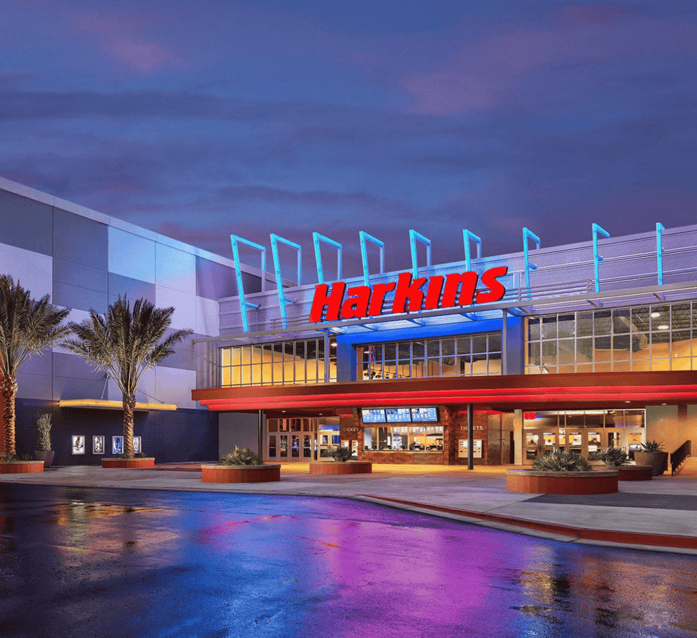 Modern Harkins Cinema theater with neon signage and palm trees outdoor at dusk, perfect for entertainment and movies.