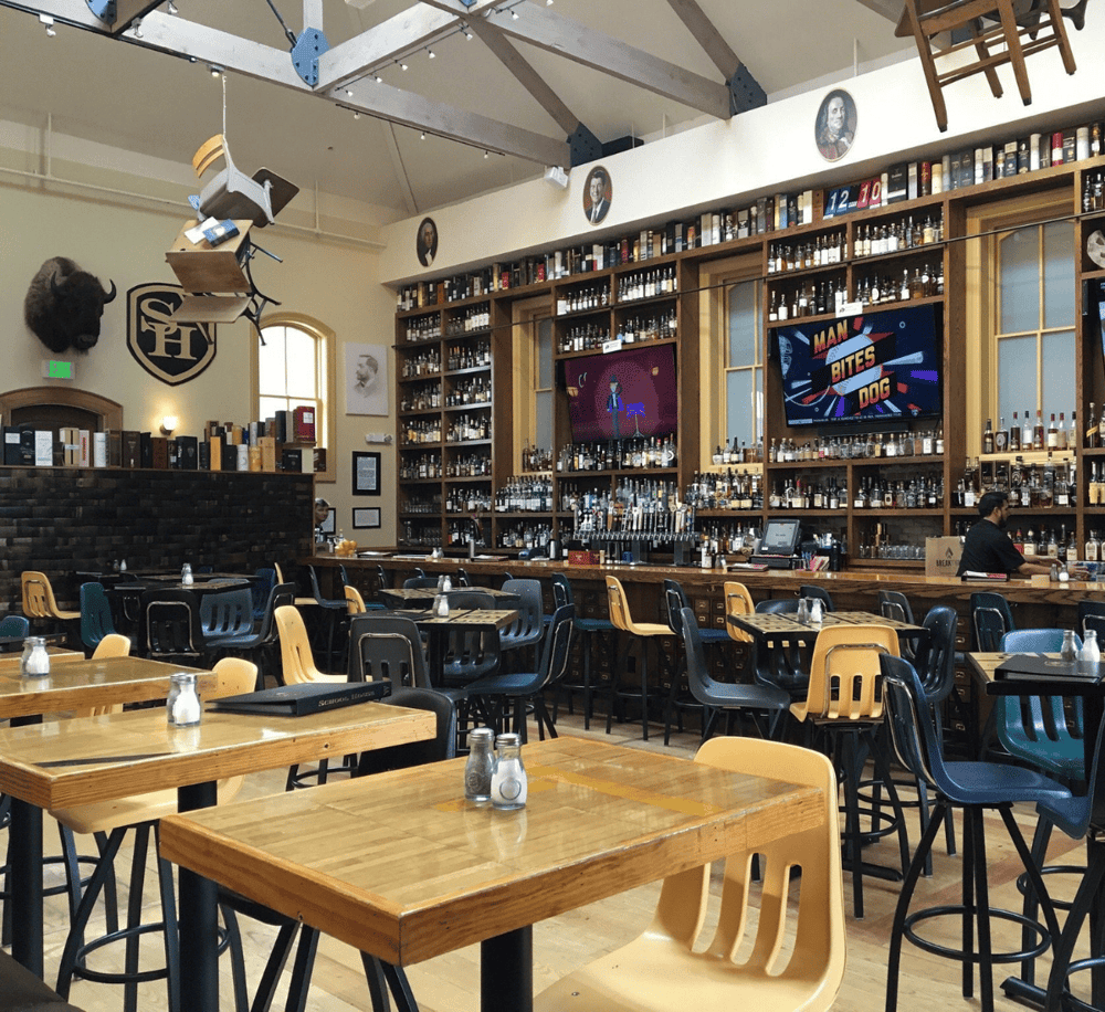 Stylish bar and restaurant interior with wooden furniture, liquor shelves, and entertainment TVs.