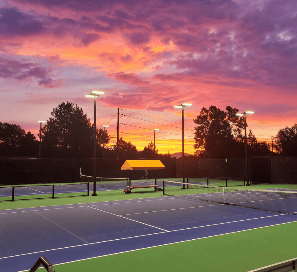 Vibrant sunset at outdoor tennis courts with lighting and colorful evening sky.