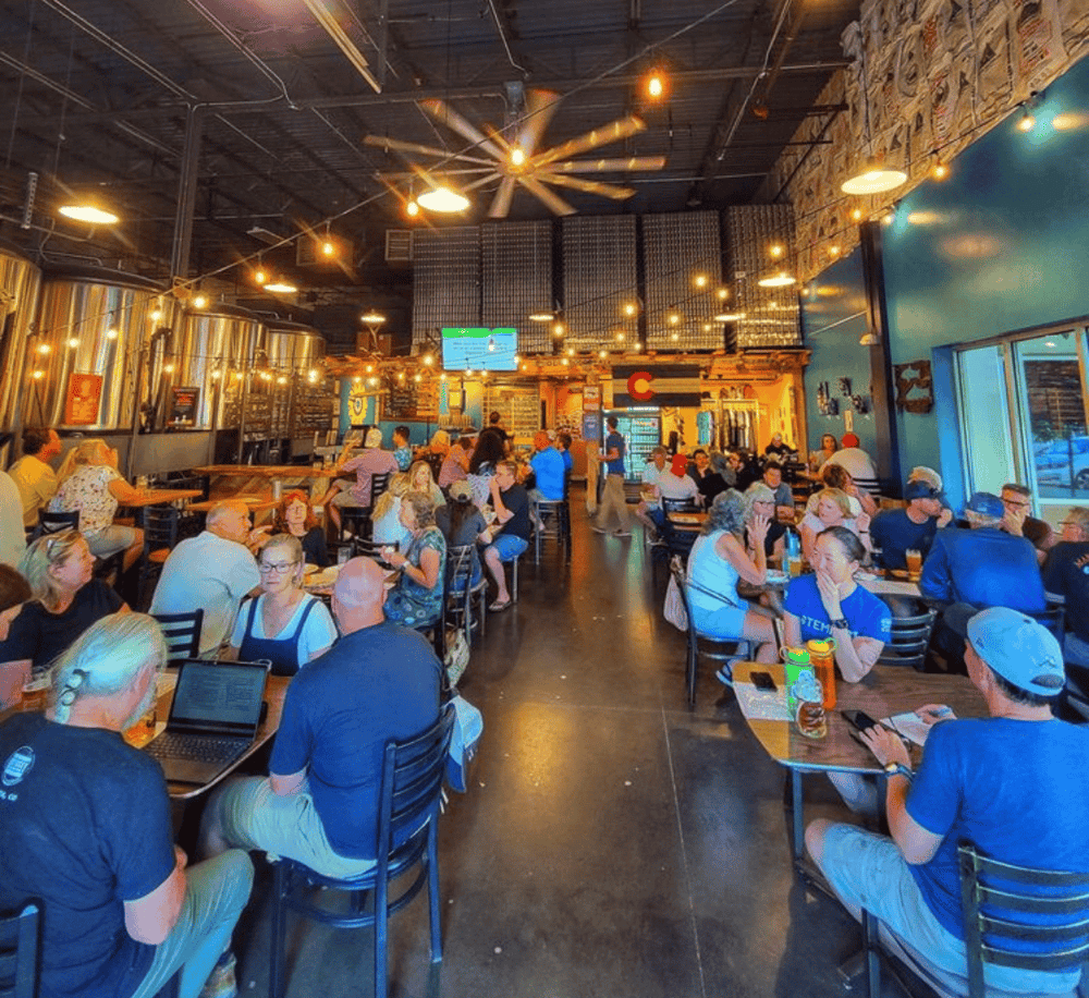 Cozy brewery with patrons enjoying craft beers and socializing, featuring vibrant industrial decor and warm lighting.