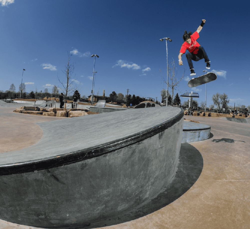 Skateboarder performing tricks at an outdoor skatepark under a clear blue sky.