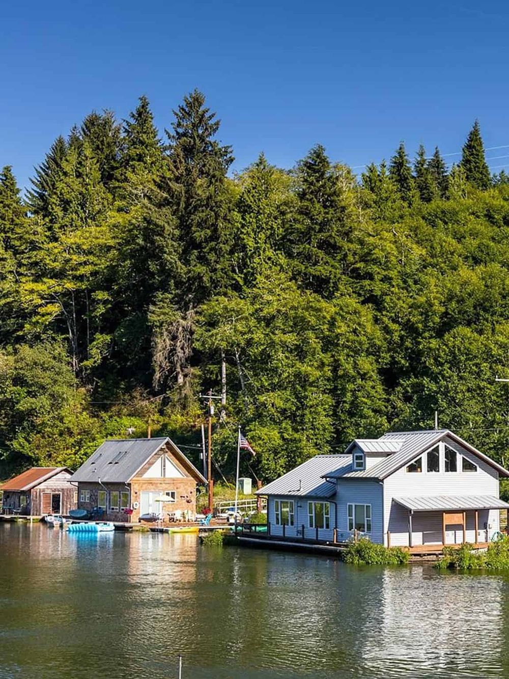 Serene lakeside scene with cozy waterfront cabins surrounded by lush green trees and clear blue sky.