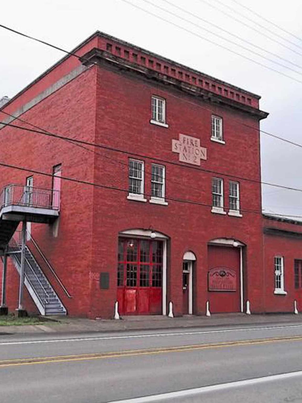 Old fire station building in red brick, with fire station sign, fire truck door, and exterior staircase.