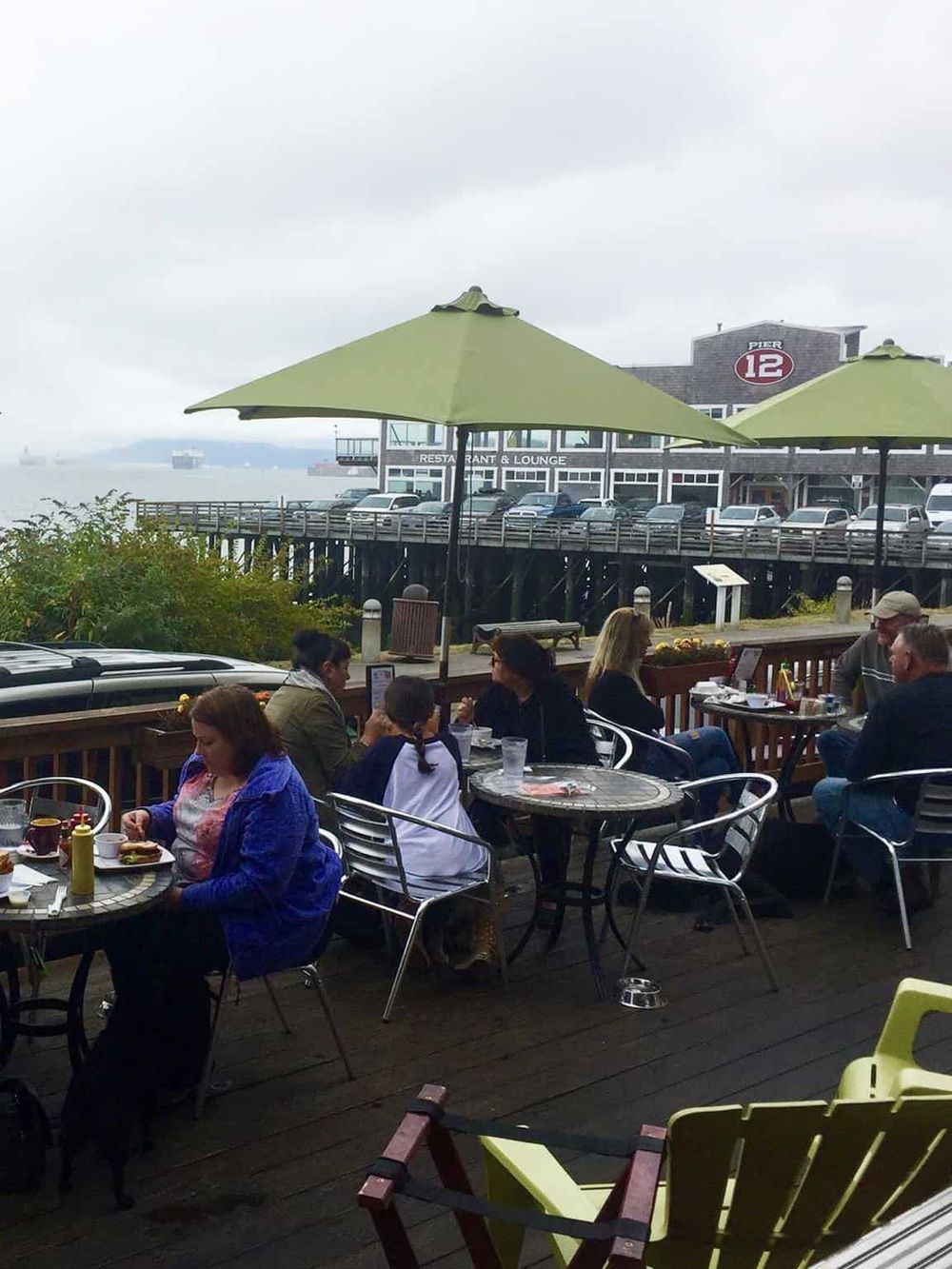 Outdoor dining at waterfront restaurant with scenic pier and harbor views.