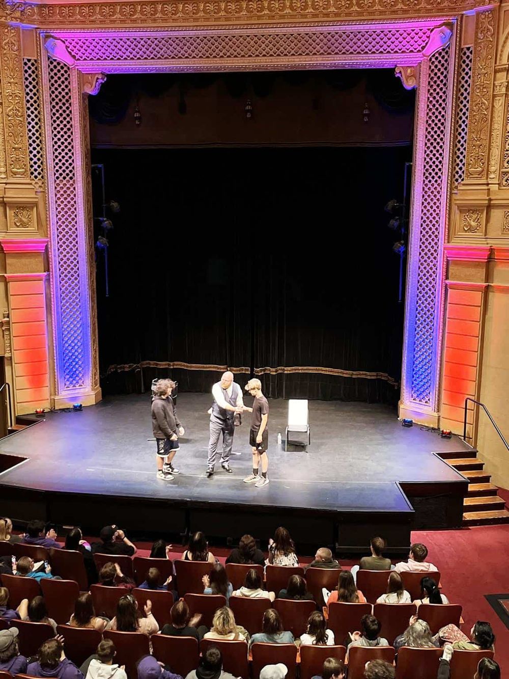 Performers on stage during a live show at Quest For Directions theater, with an engaged audience watching.