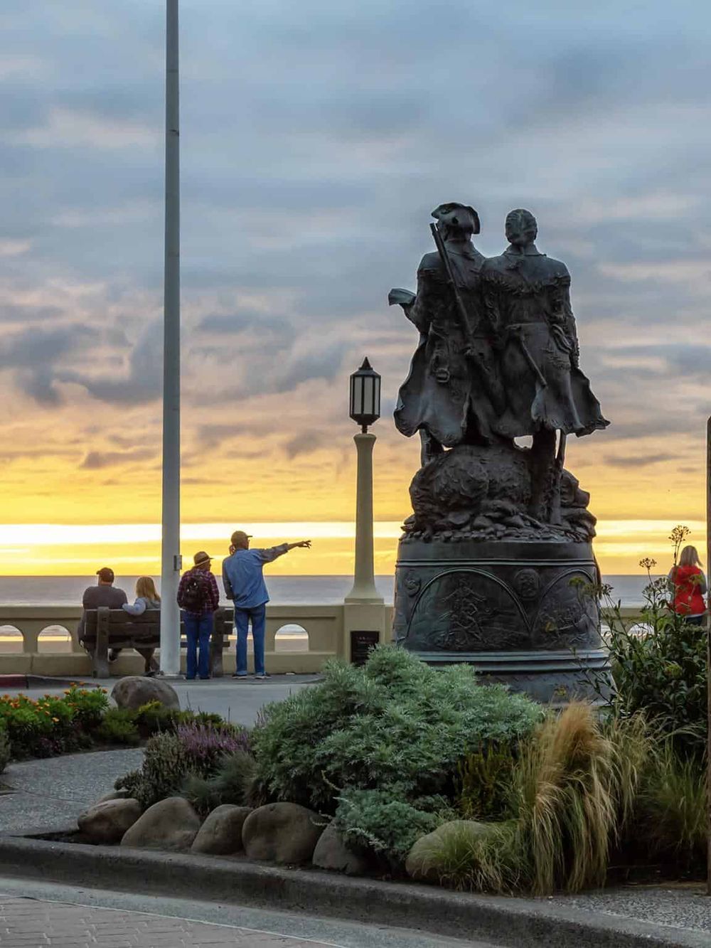 Statue of explorers overlooking the ocean at sunset, symbolizing adventure and discovery.
