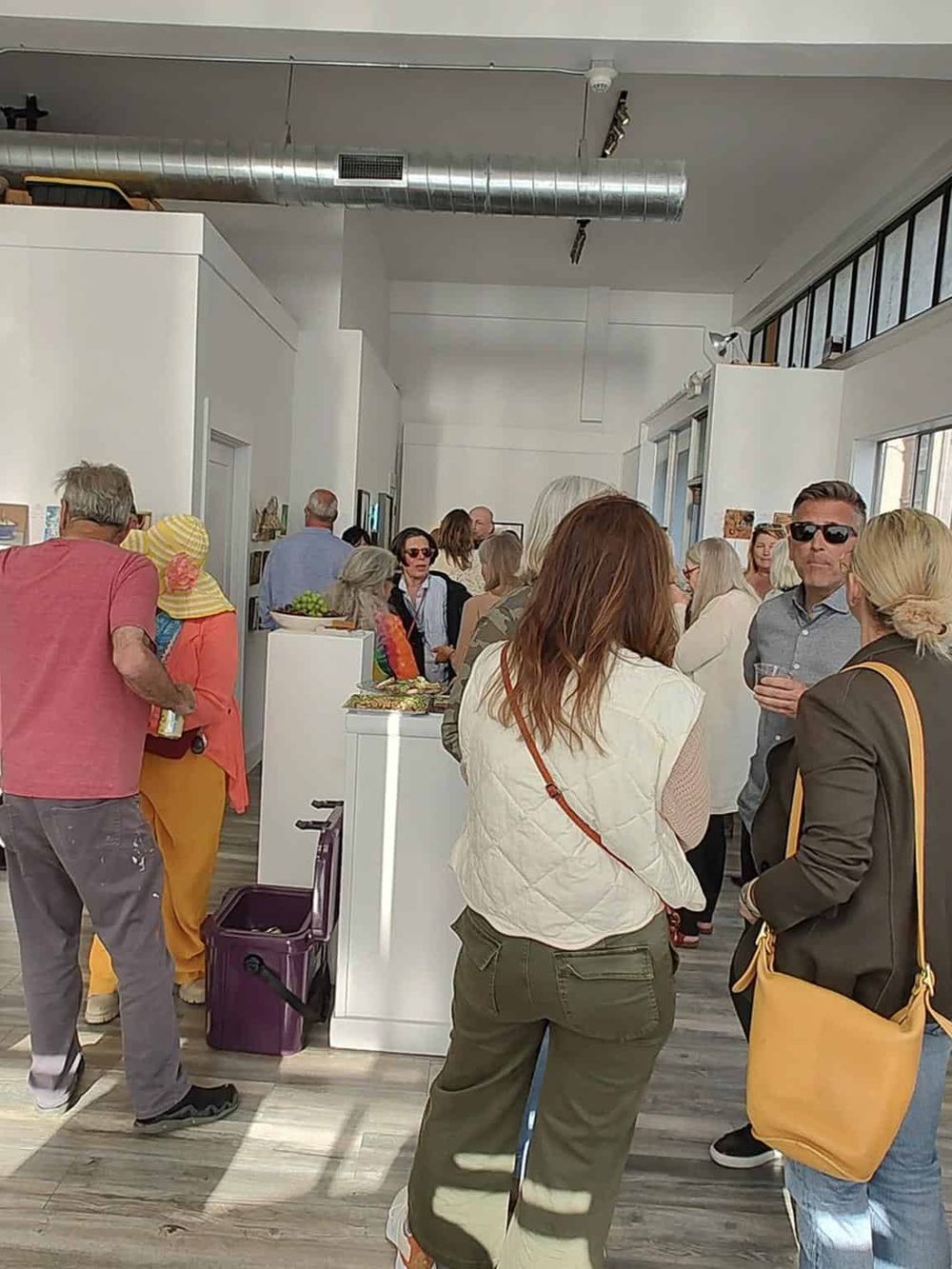People socializing at an art gallery event, modern interior with white walls and natural light.