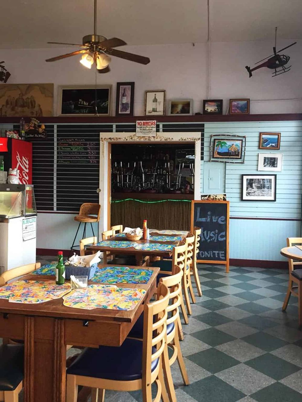 Cozy restaurant interior with tropical-themed decor, colorful table settings, and wall art, inviting for dining and live music entertainment.