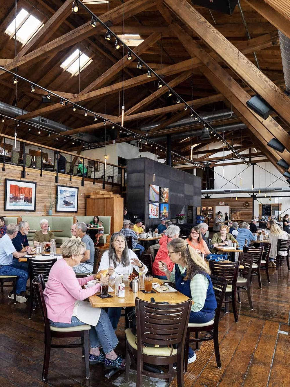Cozy restaurant interior with wooden beams and skylights, bustling with diverse diners enjoying meals.