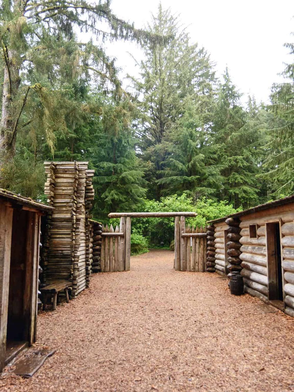 Rustic wooden fort entrance surrounded by tall green trees, natural outdoor setting.