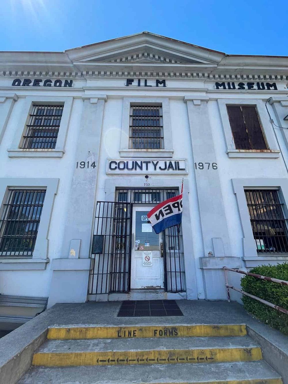 Historic Oregon County Jail building with "OPEN" sign and flag, now part of the Oregon Film Museum.