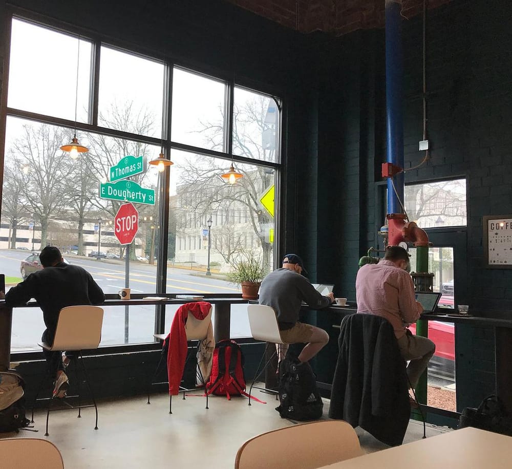 Neighborhood coffee shop interior with large windows and city street view.